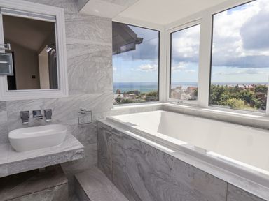 A bathroom with a bathtub next to large windows and a sink on a marble countertop at The Penthouse in Scarborough
