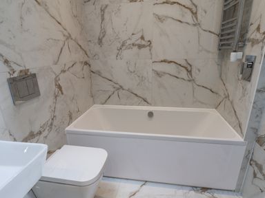A bathroom with a bathtub and toilet against marble tiled walls at The Penthouse in Scarborough