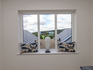 A window with two patterned cushions and a white sculpture on the sill overlooking rooftops and trees at The Penthouse in Scarborough