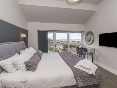 A bedroom with a made bed large window a desk chair mounted television and a circular mirror at The Penthouse in Scarborough