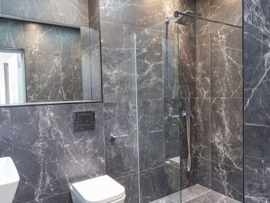 A bathroom with grey marble tiled walls and floor a white toilet a sink and a glass enclosed shower at The Penthouse in Scarborough