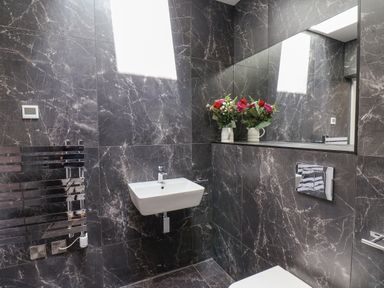 A bathroom with marble walls a wall mounted sink a towel radiator a large mirror and flowers in a vase at The Penthouse in Scarborough