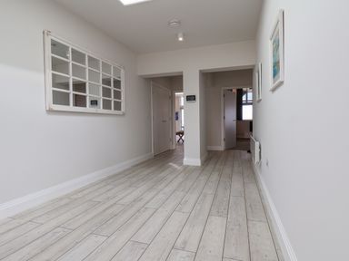 A hallway with light wood flooring a large wall mirror on the left and two framed pictures on the right at The Penthouse in Scarborough