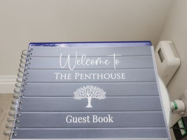 A guest book with the words Welcome to The Penthouse and a tree illustration on the cover