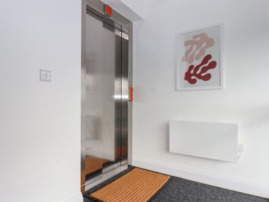 An elevator with closed doors a mat on the floor a light switch a wall heater and a framed abstract artwork on a white wall at The Penthouse in Scarborough