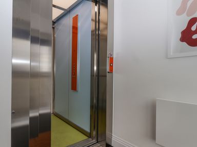 An open elevator with stainless steel doors and orange control panels inside and outside at The Penthouse in Scarborough