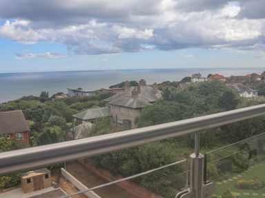 A view of residential houses and greenery with the sea in the background taken from a balcony with glass and metal railing at The Penthouse in Scarborough