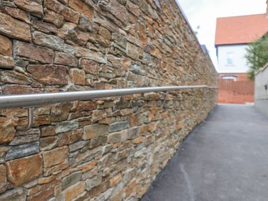 A stone wall with a metal handrail along a paved pathway leading to houses
