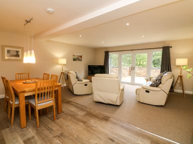 A living room and dining area with a wooden dining table and chairs and cream sofas facing a television at Spicery in Tedburn St Mary