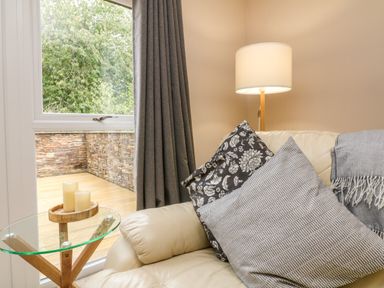 A seating area with cushions and a throw on a sofa next to a lamp and a glass side table with candles at Spicery in Tedburn St Mary