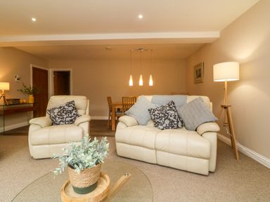 A living room with cream armchairs and sofa with cushions and a dining table with chairs at Spicery in Tedburn St Mary