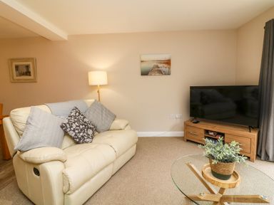 A living room with a cream sofa cushions a floor lamp a wooden TV stand with a television and a glass coffee table with a plant at Spicery in Tedburn St Mary