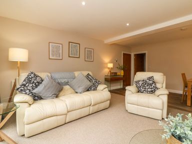 A living room with beige sofas and cushions a glass coffee table a floor lamp and framed pictures on the wall at Spicery in Tedburn St Mary