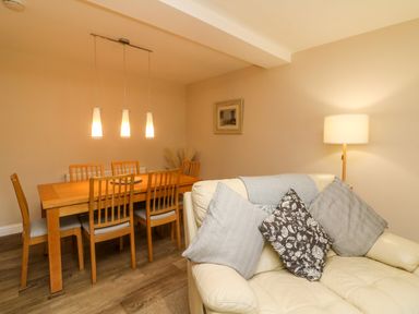 A dining area with a wooden table and six chairs next to a cream sofa with cushions and a lamp in the corner at Spicery in Tedburn St Mary