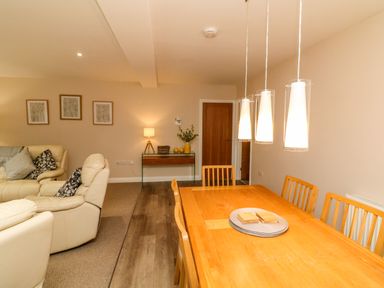 A dining room with a wooden table and chairs and a living area with cream sofas and cushions at Spicery in Tedburn St Mary