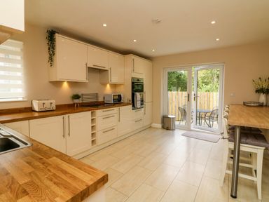 A kitchen with wooden countertops white cabinets a toaster microwave and dining area with chairs and patio doors at Spicery in Tedburn St Mary