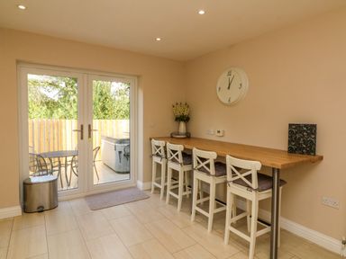 A dining area with four white chairs and a wooden countertop next to glass doors leading to an outdoor patio at Spicery in Tedburn St Mary