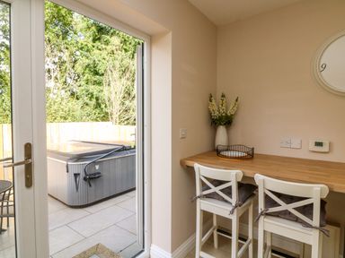 A kitchen area with wooden counter and two white chairs next to a glass door leading to a patio with a hot tub at Spicery in Tedburn St Mary