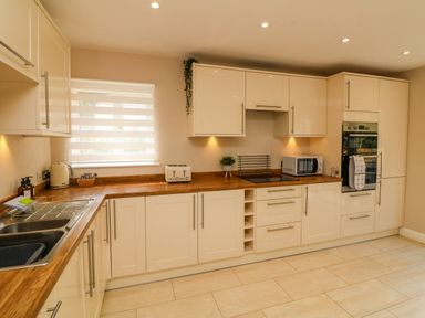 A kitchen with white cabinets wooden countertops a double sink a toaster kettle microwave and oven at Spicery in Tedburn St Mary