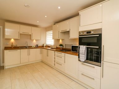 A kitchen with cream cabinets wooden countertops double ovens microwave and tiled floor at Spicery in Tedburn St Mary