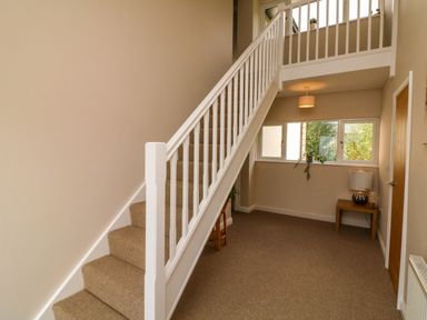 A hallway with carpeted stairs and a wooden side table with a lamp at Spicery Tedburn St Mary