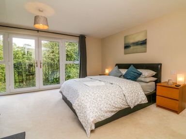 A bedroom with a bed next to two bedside tables and large windows showing trees at Spicery in Tedburn St Mary