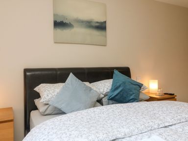 A bedroom with a double bed with patterned bedding and pillows with bedside tables and a lamp at Spicery in Tedburn St Mary