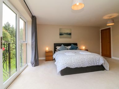 A bedroom with a bed two bedside tables with lamps a door and large window with curtains at Spicery Tedburn St Mary