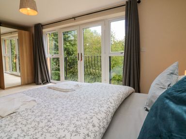 A bedroom with a bed covered with patterned bedding and pillows near a window with curtains and a wardrobe with a mirrored door at Spicery in Tedburn St Mary