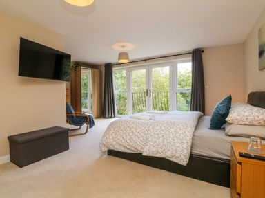 A bedroom with a double bed side table a wall mounted television armchair and glass doors with curtains at Spicery in Tedburn St Mary