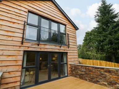 The exterior of a wooden house with black framed windows and doors and a stone wall on a deck at Spicery in Tedburn St Mary