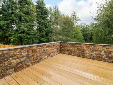 A wooden deck with stone wall surround and trees in the background at Spicery in Tedburn St Mary