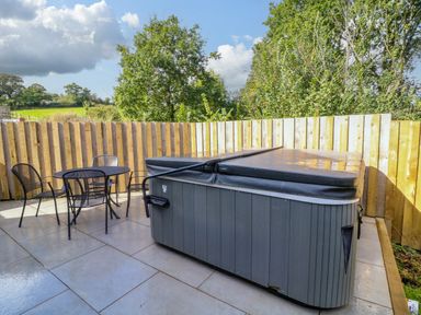 An outdoor patio with a covered hot tub and a round table with four chairs surrounded by a wooden fence at Spicery in Tedburn St Mary