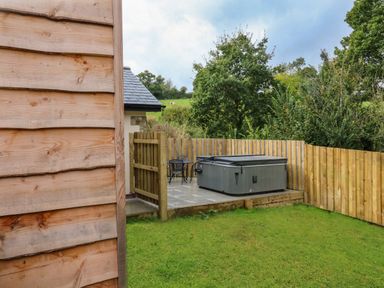 An outdoor area with a wooden fence a hot tub a small table with two chairs and grass at Spicery in Tedburn St Mary