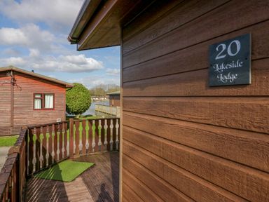 A wooden lodge exterior with a sign reading 20 Lakeside Lodge near wooden railing and a body of water at Lakeside 20 in Warton near Carnforth