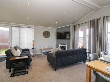 A living room with two sofas a wall clock a television and curtains at Lakeside 20 in Warton near Carnforth