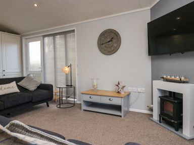 A living room with a sofa an end table with a lamp a wall clock and a fireplace at Lakeside 20 Warton near Carnforth