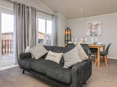 A living room with a black sofa and dining table set with plates and glasses at Lakeside 20 in Warton near Carnforth