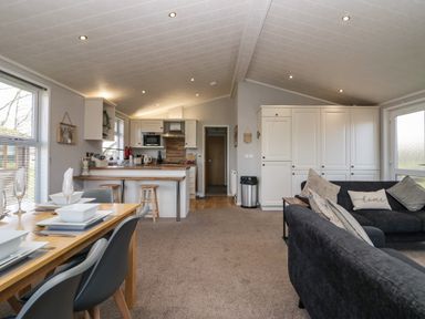 An open-plan living space with a dining table set for four a kitchen with bar stools on carpeted floor and a black sofa with cushions at Lakeside 20 in Warton near Carnforth