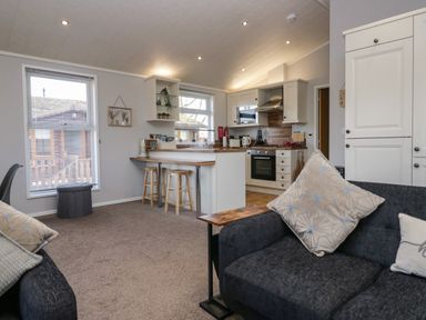 A living room with a sofa and kitchen with stools and cabinets at Lakeside 20 in Warton near Carnforth