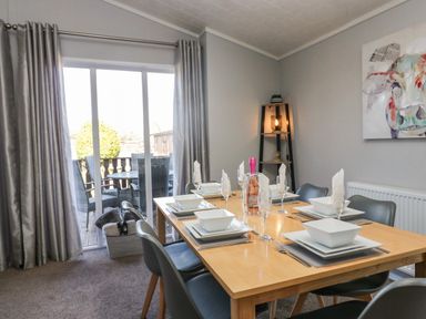 A dining room with a set table and chairs near sliding glass doors at Lakeside 20 in Warton near Carnforth