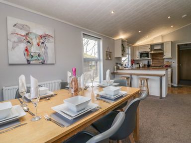 A dining table set with plates glasses and a bottle in a kitchen dining area with stools at Lakeside 20 in Warton near Carnforth