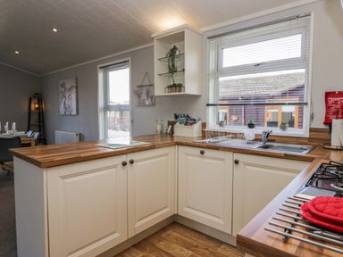 A kitchen with white cabinets wooden countertops a sink with a drying rack and small potted plants on the windowsill at Lakeside 20 in Warton near Carnforth
