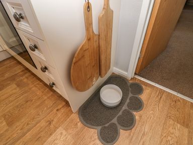 A kitchen corner with wooden cutting boards hanging on the wall and a grey paw-shaped mat with a white bowl on a wooden floor at Lakeside 20 in Warton near Carnforth