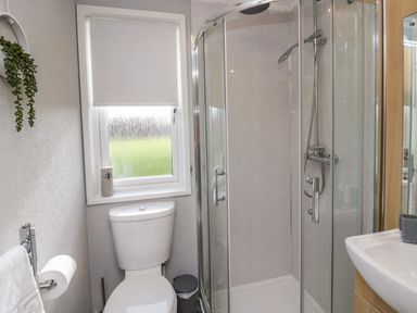 A bathroom with a toilet, shower enclosure, sink, window with blind, and wall-mounted towel holder at Lakeside 20 in Warton near Carnforth