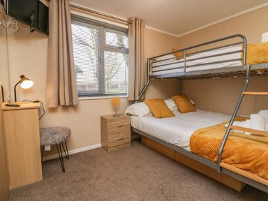 A bedroom with a bunk bed a bedside table with lamp a window and a wall-mounted tv at Lakeside 20 in Warton near Carnforth
