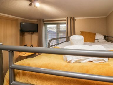 A bedroom with a bunk bed covered with yellow blankets and white towels a window with blinds a mounted tv and a wooden door at Lakeside 20 in Warton near Carnforth