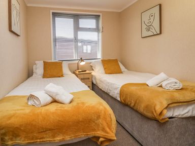 A bedroom with two single beds with orange blankets and pillows at Lakeside 20 in Warton near Carnforth