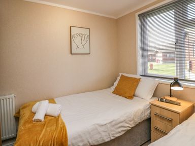 A bedroom with two single beds a nightstand with a lamp and remote and a window with blinds at Lakeside 20 in Warton near Carnforth