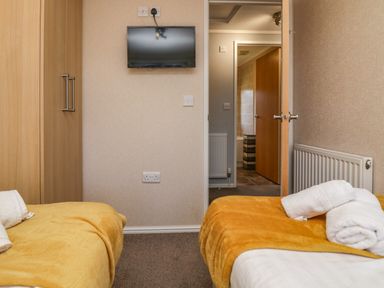 A bedroom with two single beds with yellow blankets a wall mounted tv and an open door showing a corridor at Lakeside 20 Warton near Carnforth